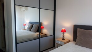 Een hotelkamer met een spiegelkast, een bed met een witte dekbedovertrek, twee nachtkastjes met rode lampen en een houten hoofdbord.