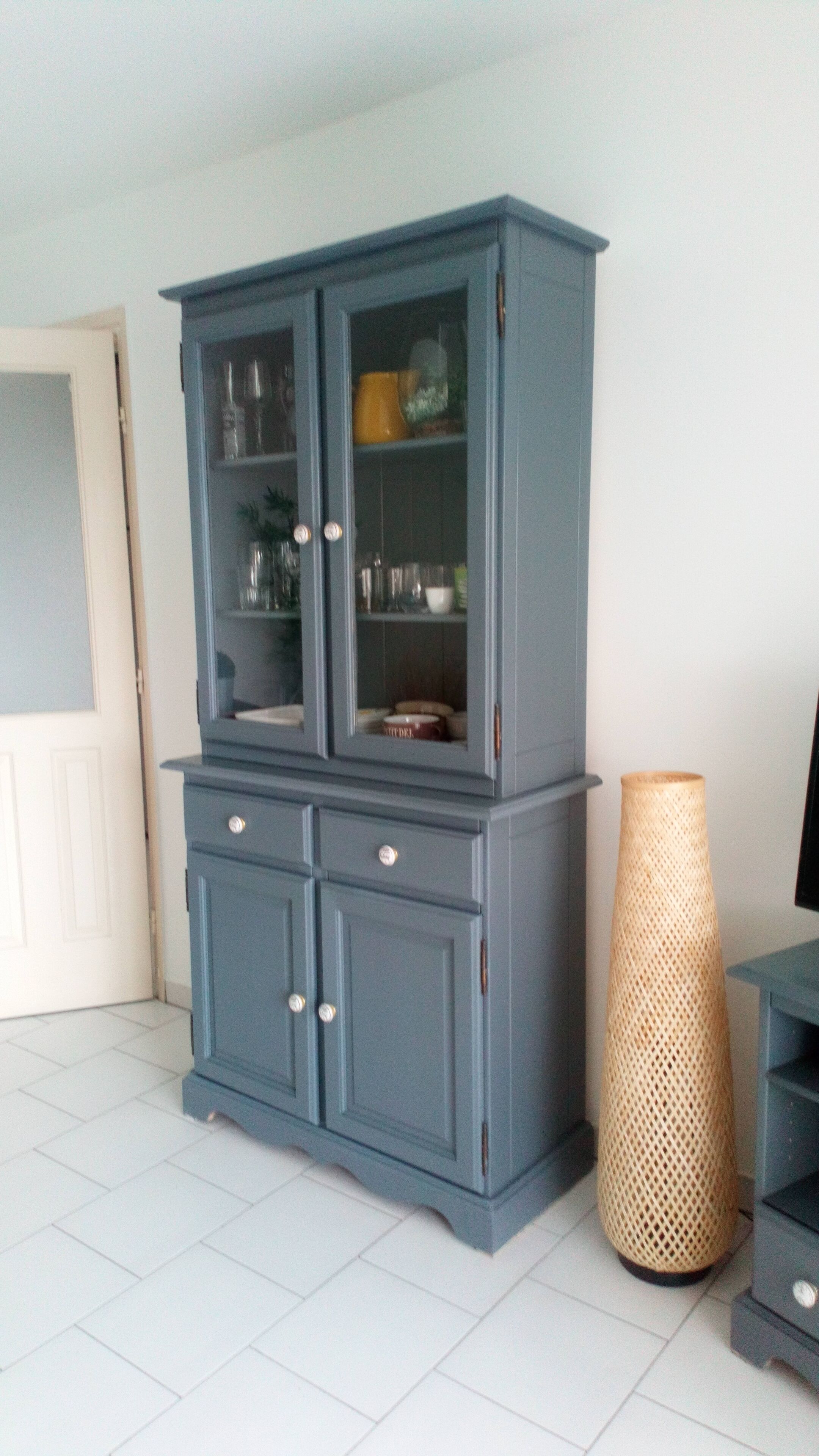 A blue cabinet with glass doors and drawers, a wicker basket, and a white tiled floor.