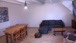 Uma sala de estar com uma mesa de jantar de madeira, um sofá escuro, uma mesa de centro e uma escada.