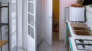 Cozinha com fogão a gás, pia e bancada. Há uma porta que dá para outro cômodo.