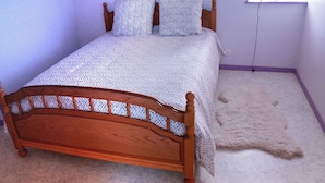 Quarto com cama de madeira, roupa de cama estampada, um globo na janela e um tapete de pele no chão.