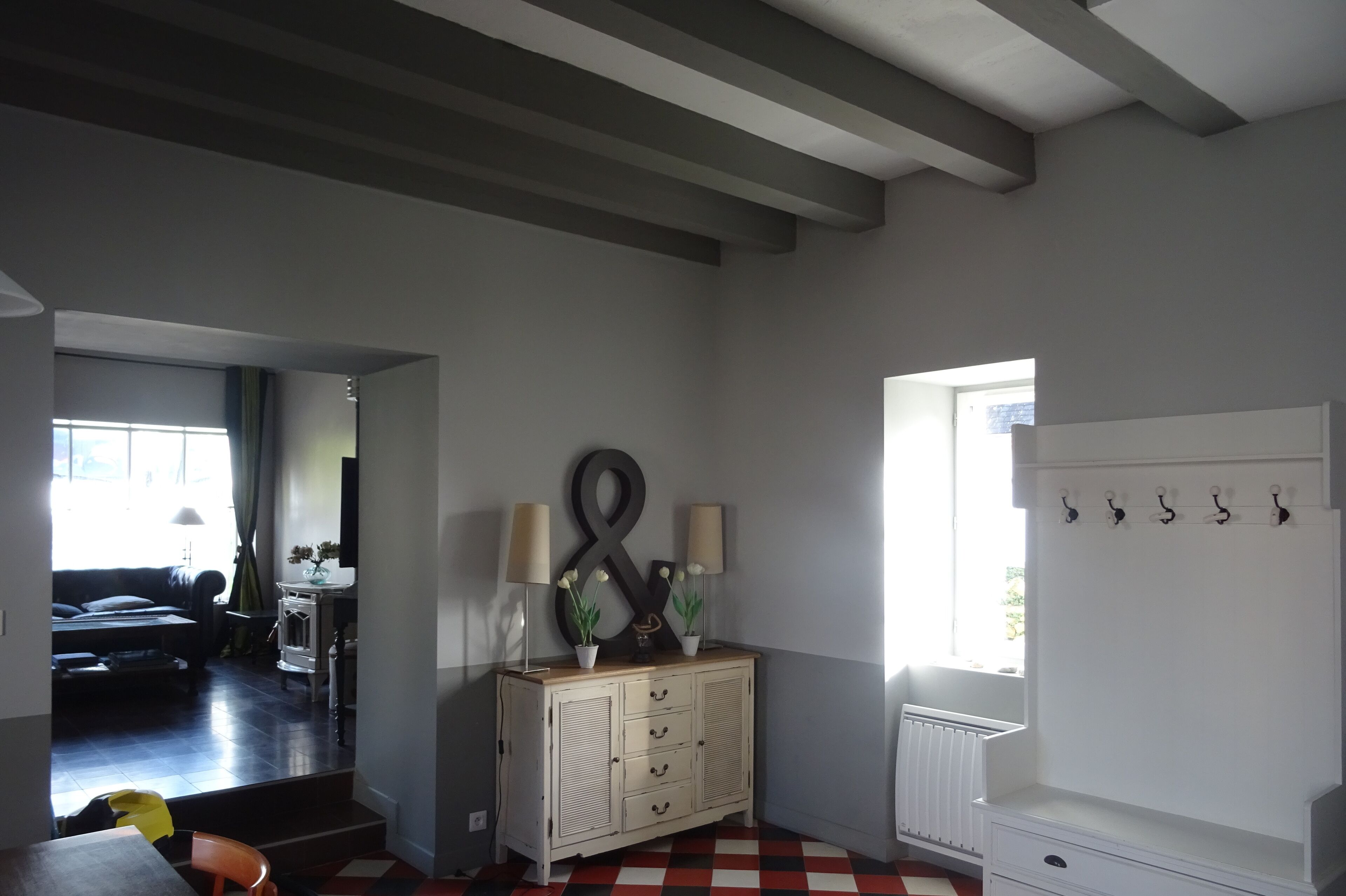 Une pièce avec un radiateur blanc, un meuble en bois doté de tiroirs, un porte-manteau et une grande fenêtre avec des rideaux.