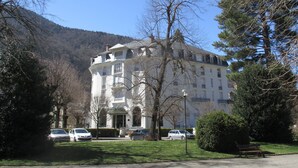 A large, multi-story building with a symmetrical facade, surrounded by trees and a mountain in the background.