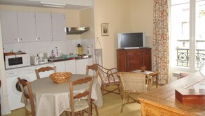 A compact kitchen with white cabinets, a microwave, and a coffee maker. There's a dining table with chairs and a television on a wooden cabinet.