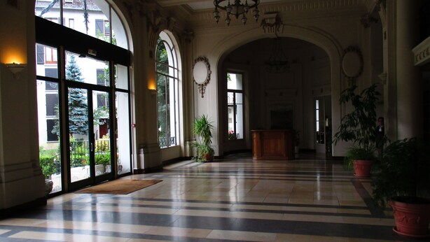 A spacious lobby with large arched windows, a checkered floor, and a wooden reception desk.