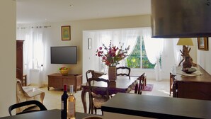 Ein Essbereich mit Tisch, Stühlen, einer Blumenvase, einem Fernseher und einem Fenster mit Vorhängen.