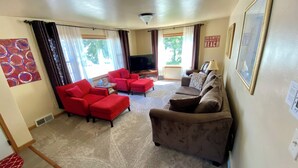 A living room with a sofa set, a TV, and a large window with curtains. - The Sister Bay Getaway: Water View & Downtown! Come enjoy Door County! (Sister Bay)