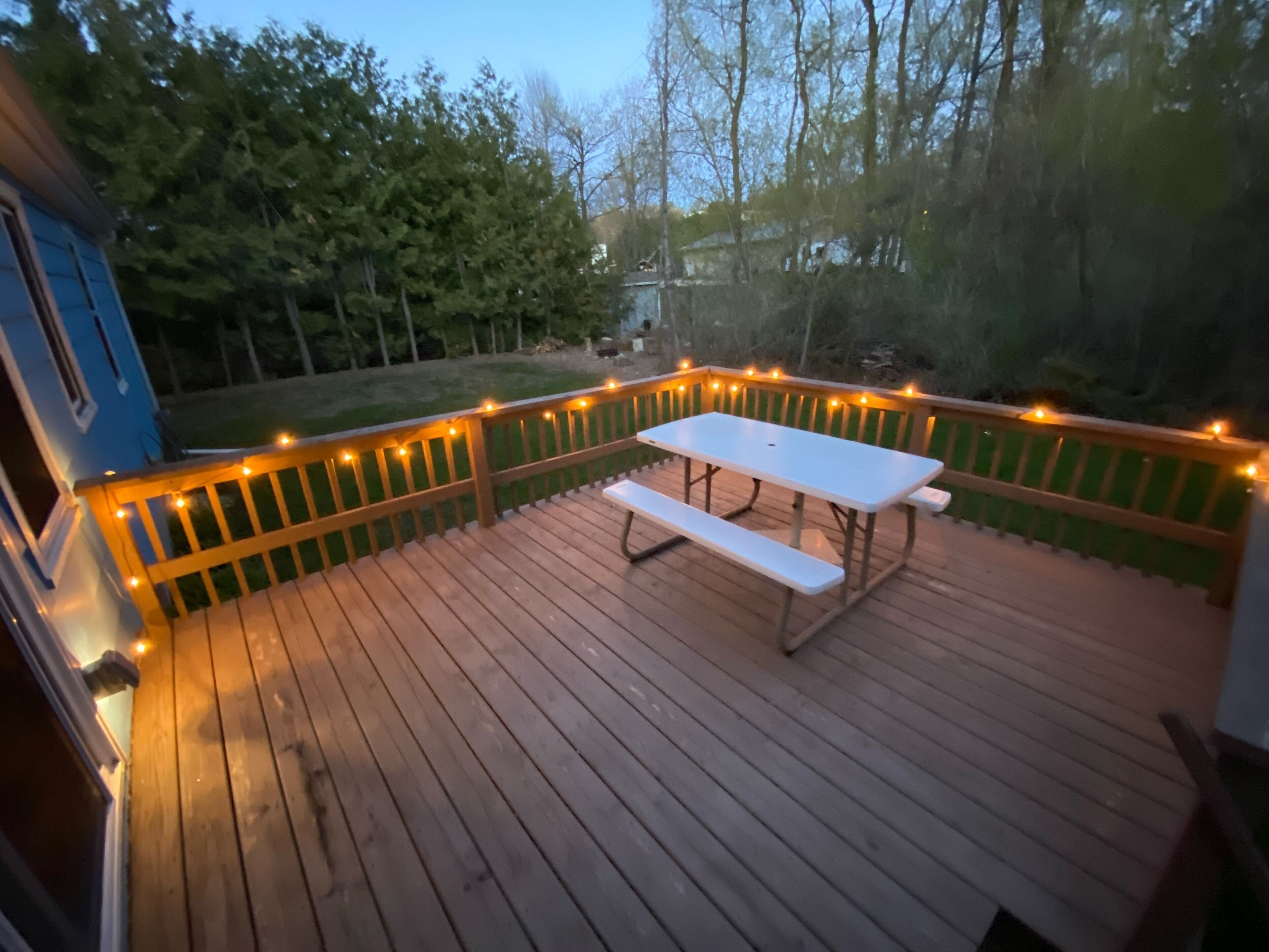 Une terrasse en bois avec une table de pique-nique et des guirlandes lumineuses.
