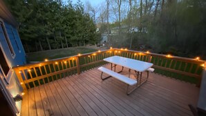 A wooden deck with a picnic table and string lights. - The Sister Bay Getaway: Water View & Downtown! Come enjoy Door County! (Sister Bay)