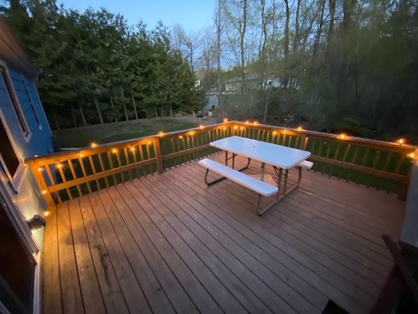Una terraza de madera con una mesa de picnic y luces colgantes.