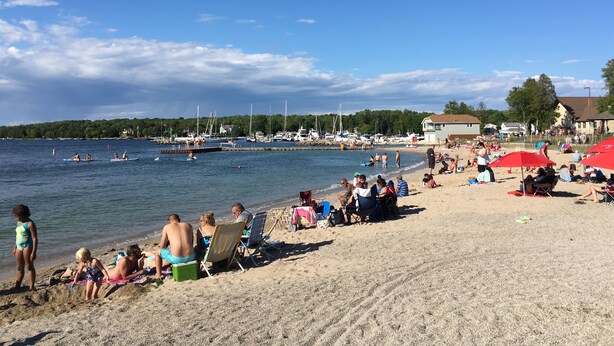A beach with people relaxing, some on the sand and others in the water. There are boats and a dock in the background. - The Sister Bay Getaway: Water View & Downtown! Come enjoy Door County! (Sister Bay)