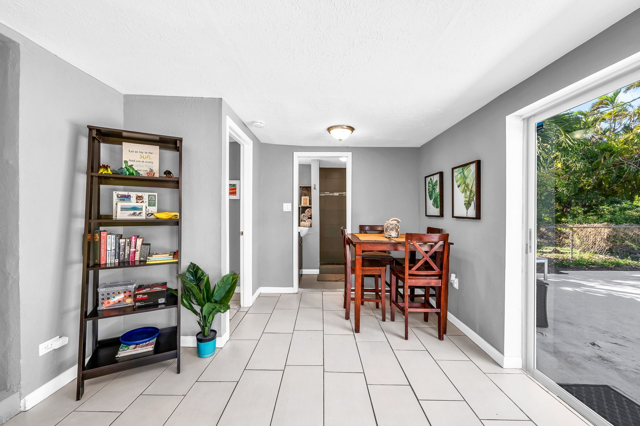 A hallway with a bookshelf, a dining table with chairs, and a view of the outdoors.