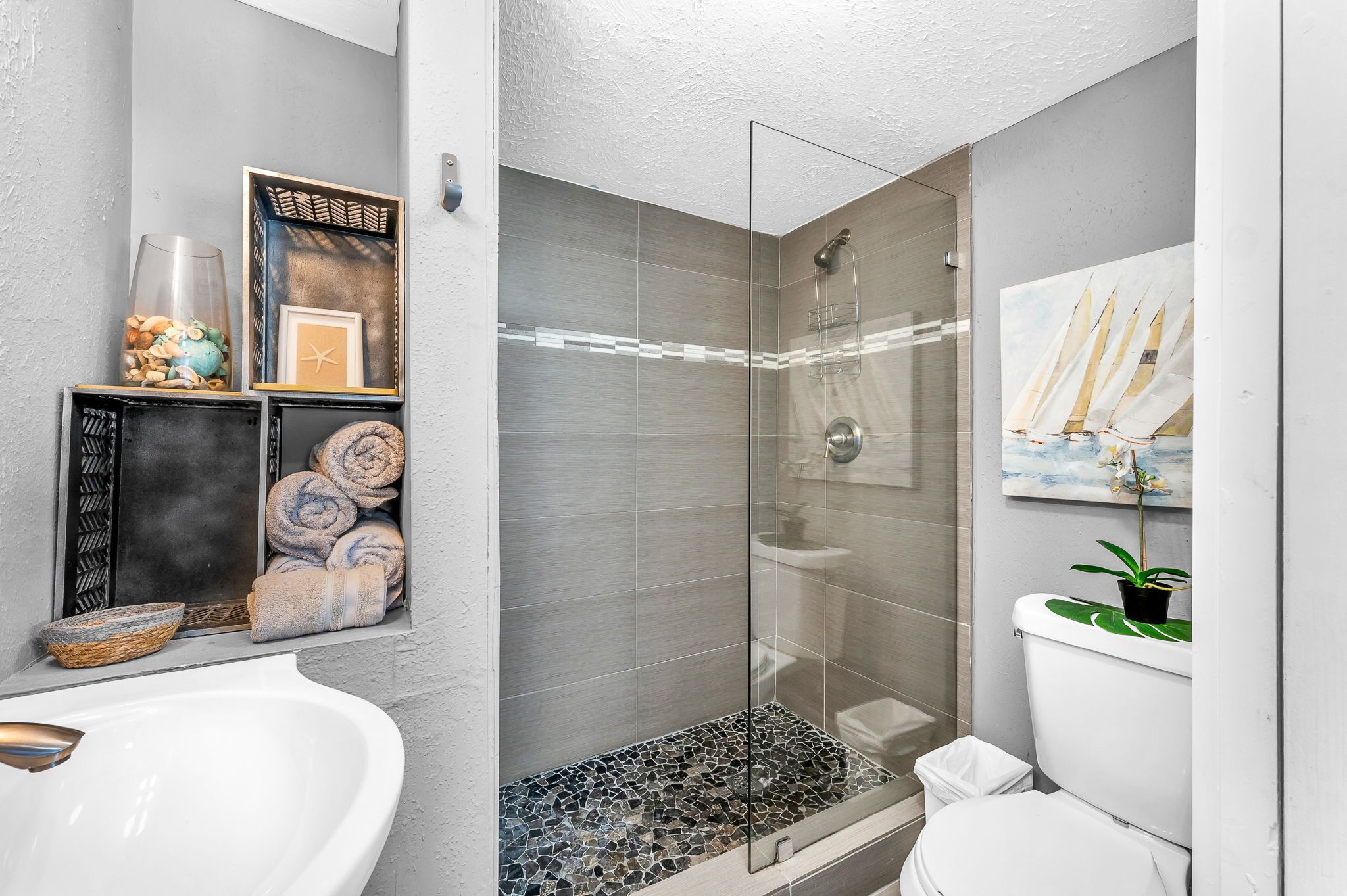 A modern bathroom with a glass shower enclosure, a white sink, and a toilet.