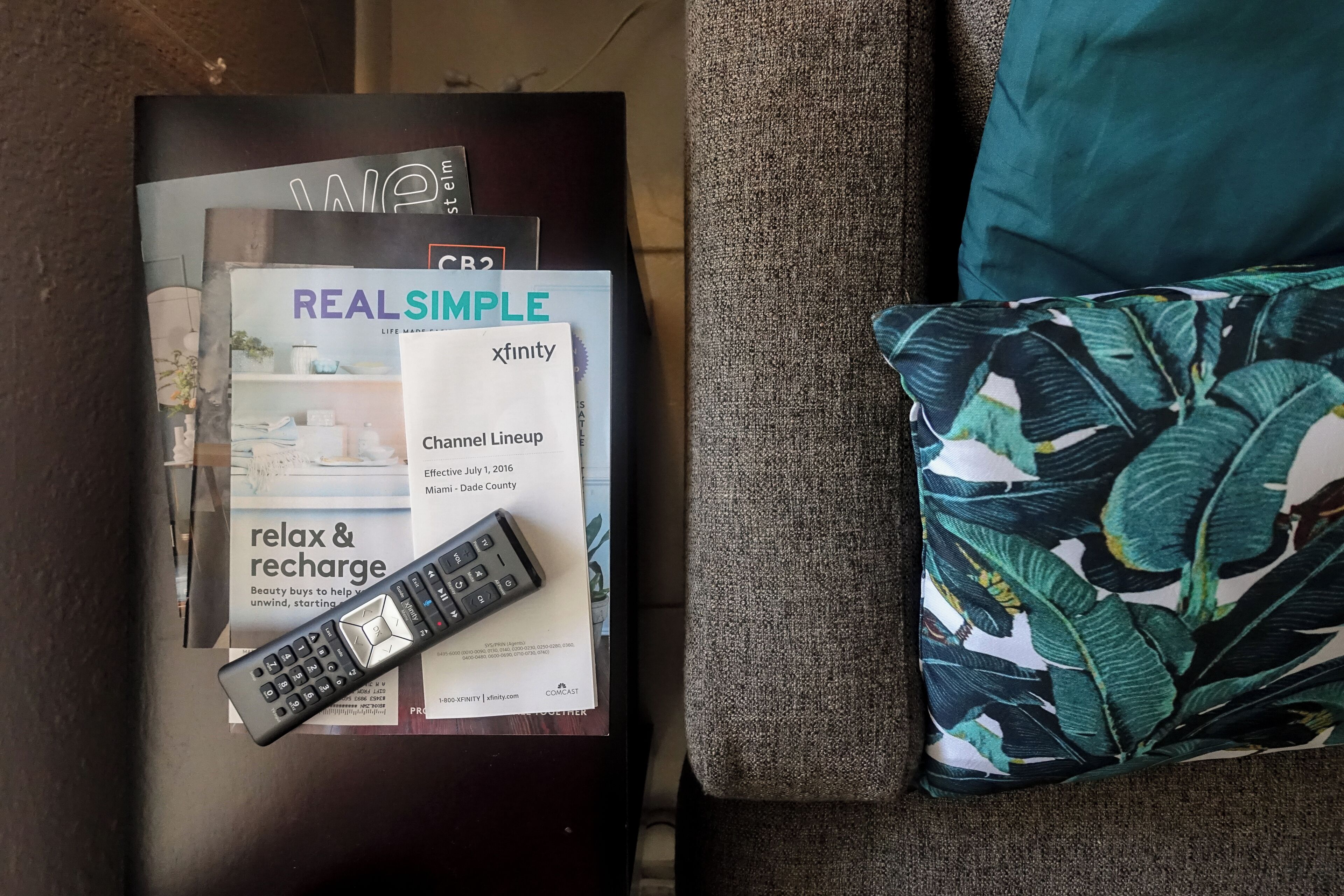 A remote control, a magazine, and a pillow on a dark surface.