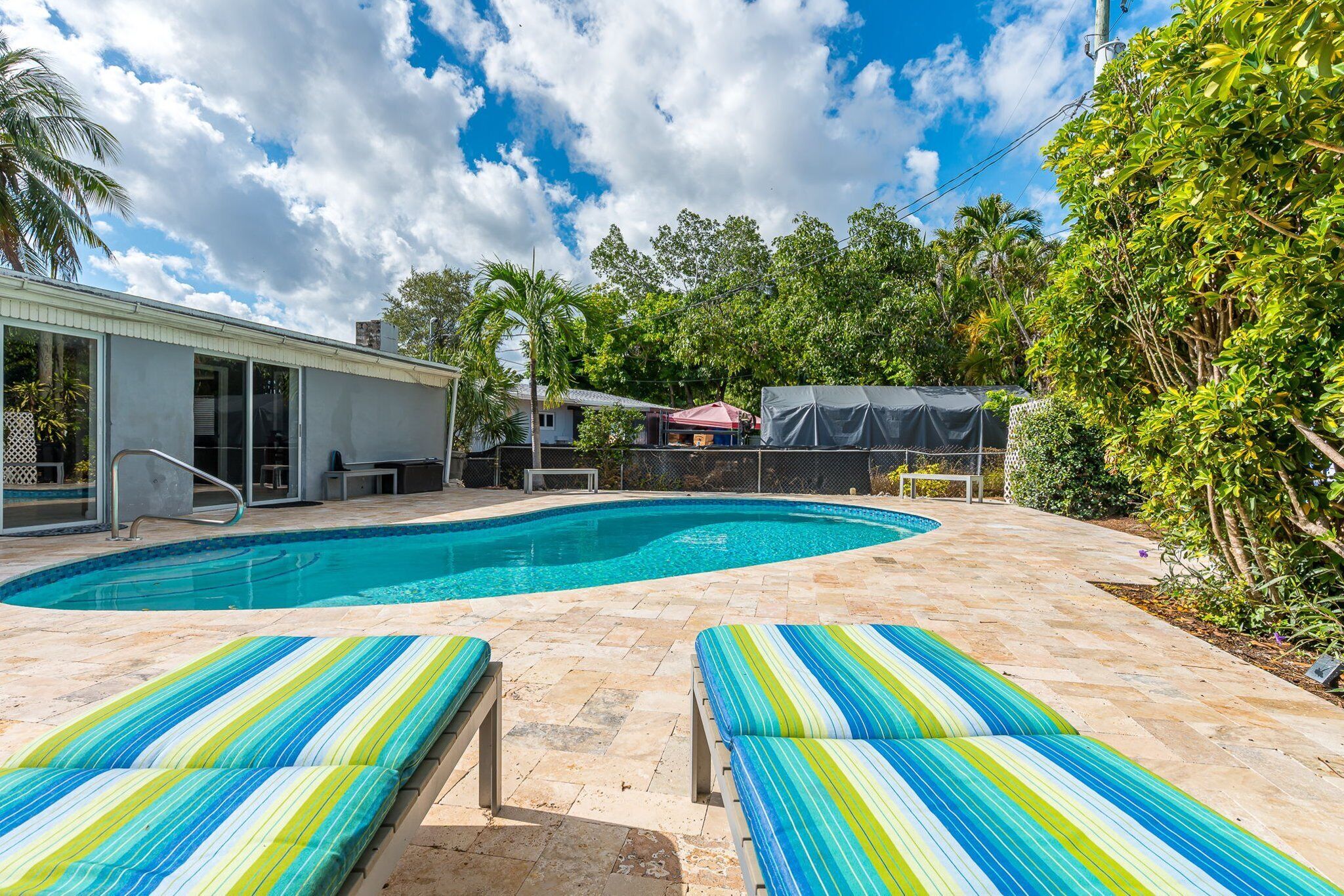 A swimming pool with lounge chairs, a covered area, and a house in the background.