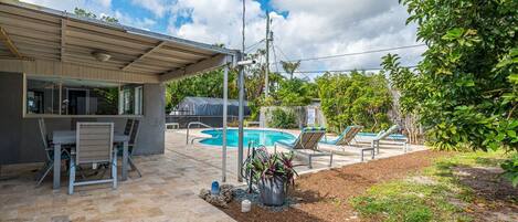 A backyard with a pool, outdoor seating, and a covered patio area.