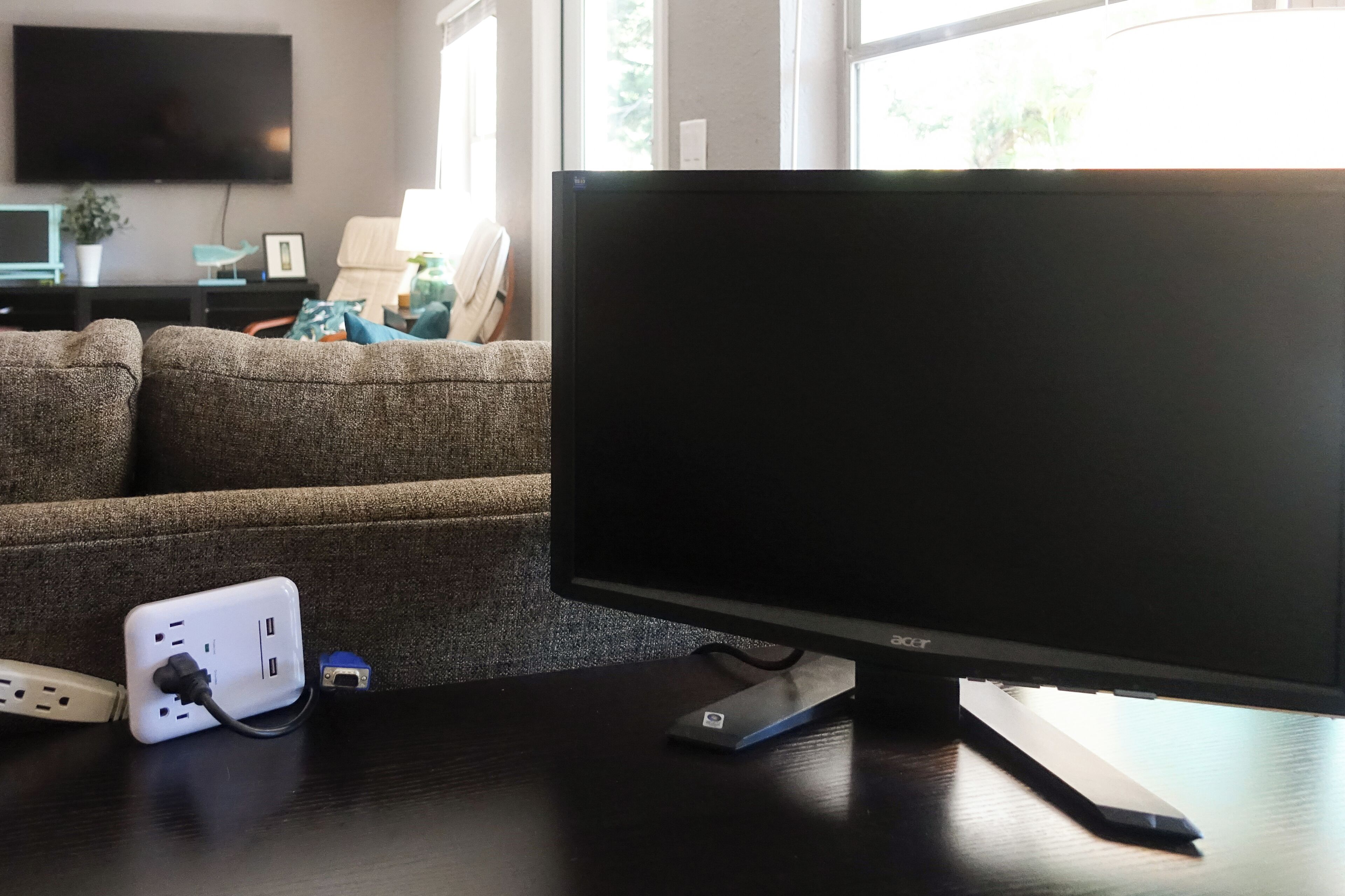 A modern living room with a large flat-screen TV, a sofa, and a table with a power strip and a small blue object.