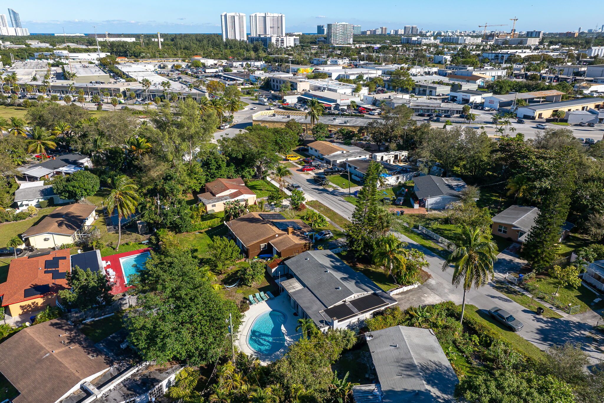 An aerial view of a residential area with houses, a swimming pool, and a clear sky.