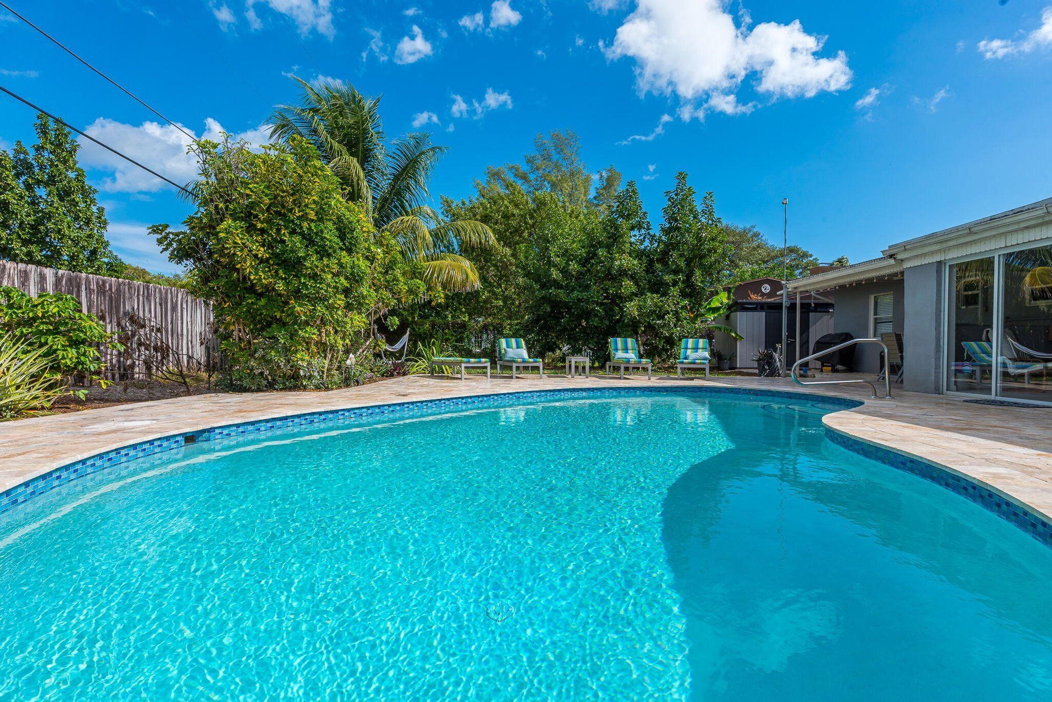 Une piscine d’un bleu éclatant, avec des chaises longues et une clôture en bois en arrière-plan.