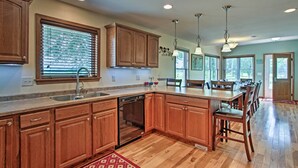 A kitchen with wooden cabinets, a dishwasher, a large island with chairs, and pendant lights.
