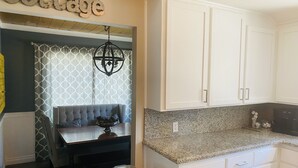 A kitchen with white cabinets, a granite countertop, and a dining area with a bench and table.