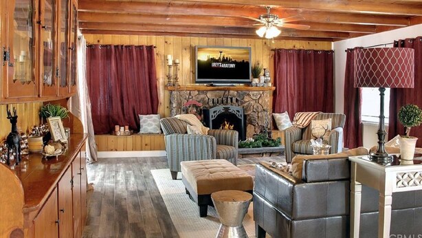 A cozy living room with a fireplace, wooden ceiling, and a television mounted above it.