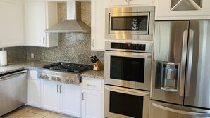 A modern kitchen with white cabinets, a stainless steel stove, an oven, a microwave, and a refrigerator.