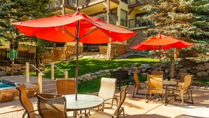 An outdoor patio area with round tables and chairs, red umbrellas, and a pool.