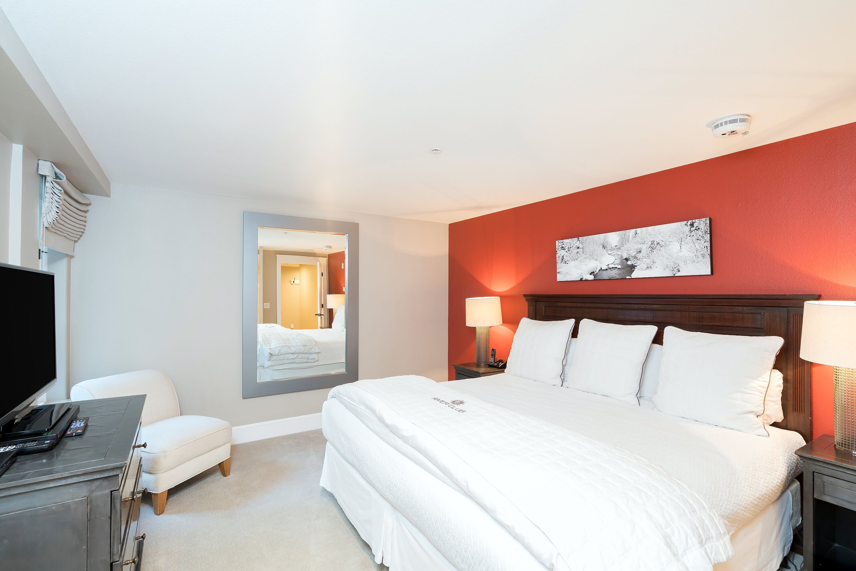 A hotel room with a large bed, a desk with a laptop, a chair, and a TV.