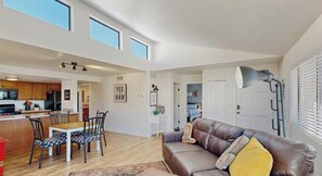 A spacious living area with a brown leather sofa, a dining table with chairs, and a kitchen in the background.