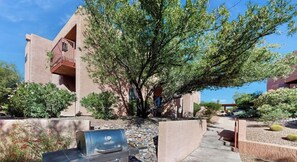 A building with a patio area, a barbecue grill, and a tree.