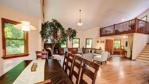 A spacious living area with a dining table, wooden chairs, a sofa, and a staircase leading to an upper level.