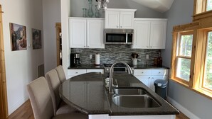Una cocina moderna con armarios blancos, encimera de granito, microondas integrado y un amplio ventanal.