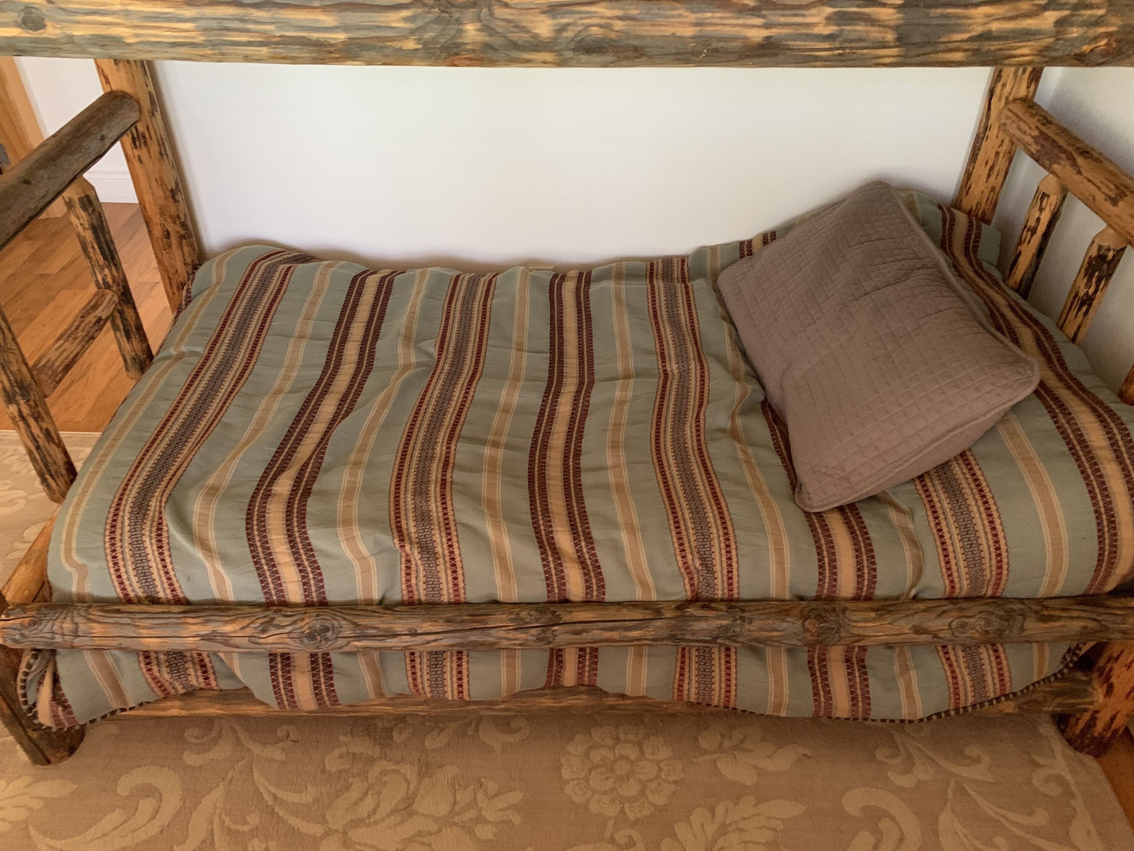 Uma cama de madeira com um edredom listrado e um único travesseiro.