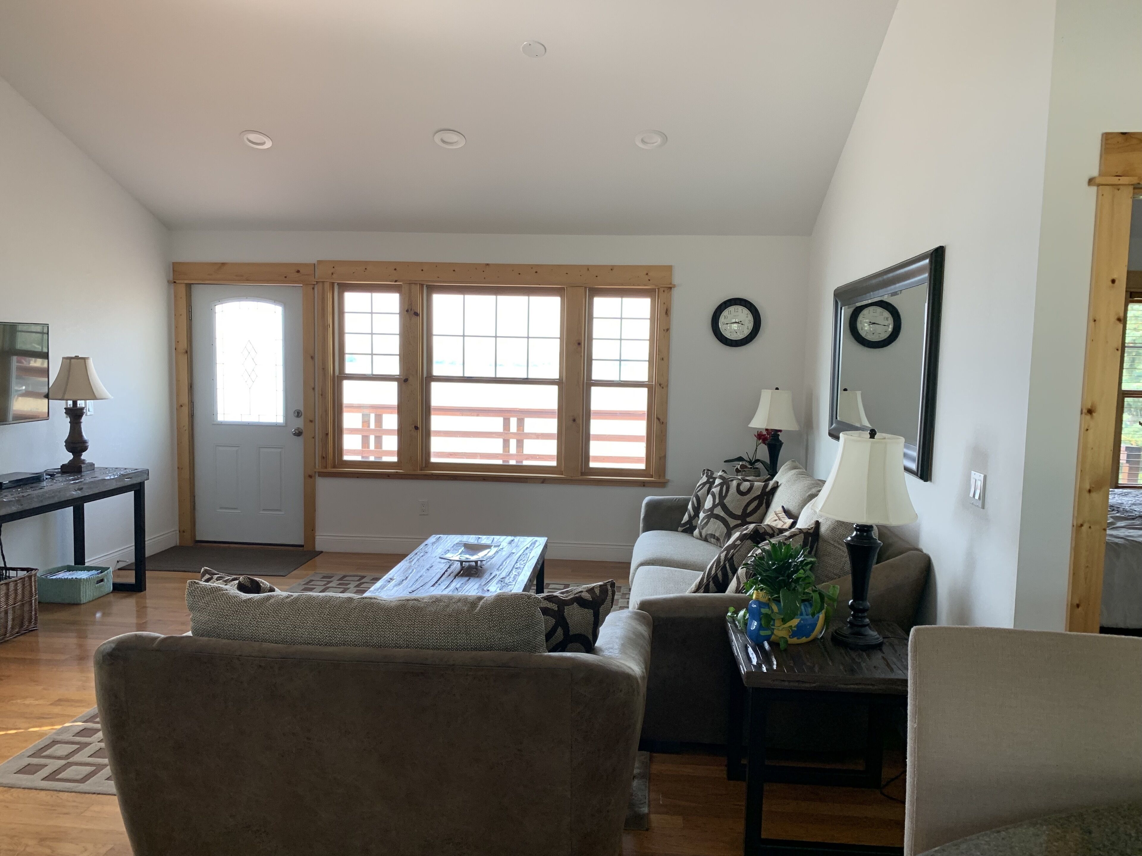 A living room with a sofa, coffee table, and lamps. There are windows with wooden frames and a door.