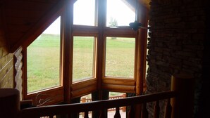 A room with a large window overlooking a grassy field. The room features wooden beams and a stone wall. - Yellowstone, Grand Teton, Fish, Ski, Parks, Pets, Bike, Fire Pit, (Freedom)