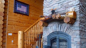 A rustic cabin interior with a stone fireplace, wooden logs, and a wooden staircase. - Yellowstone, Grand Teton, Fish, Ski, Parks, Pets, Bike, Fire Pit, (Freedom)