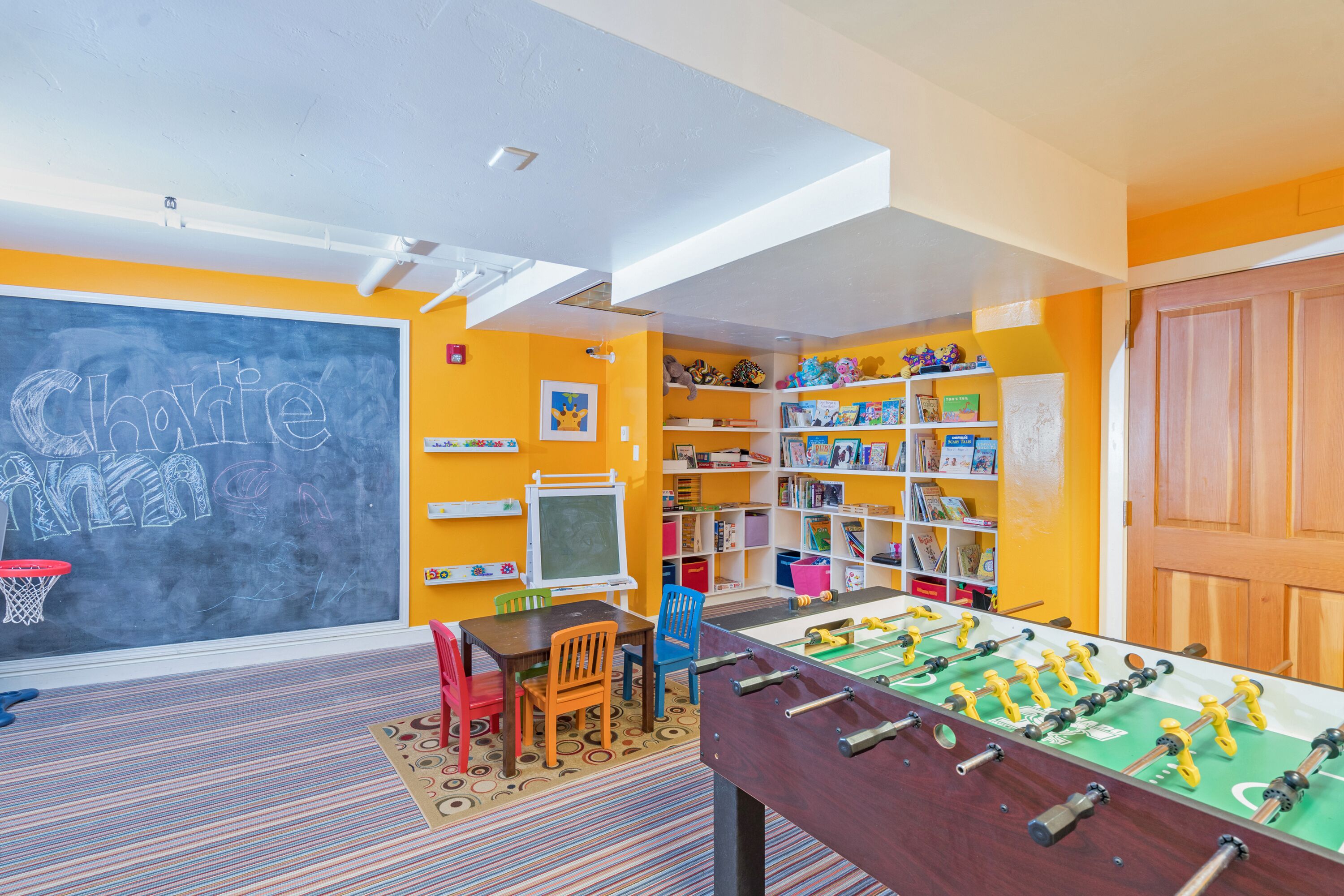 Una habitación de colores vivos con una mesa de fútbol de mesa, una pizarra con escritura y estantes llenos de juguetes y libros.