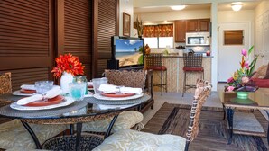 Un coin repas avec une table dressée pour deux personnes, un téléviseur et une cuisine en arrière-plan.