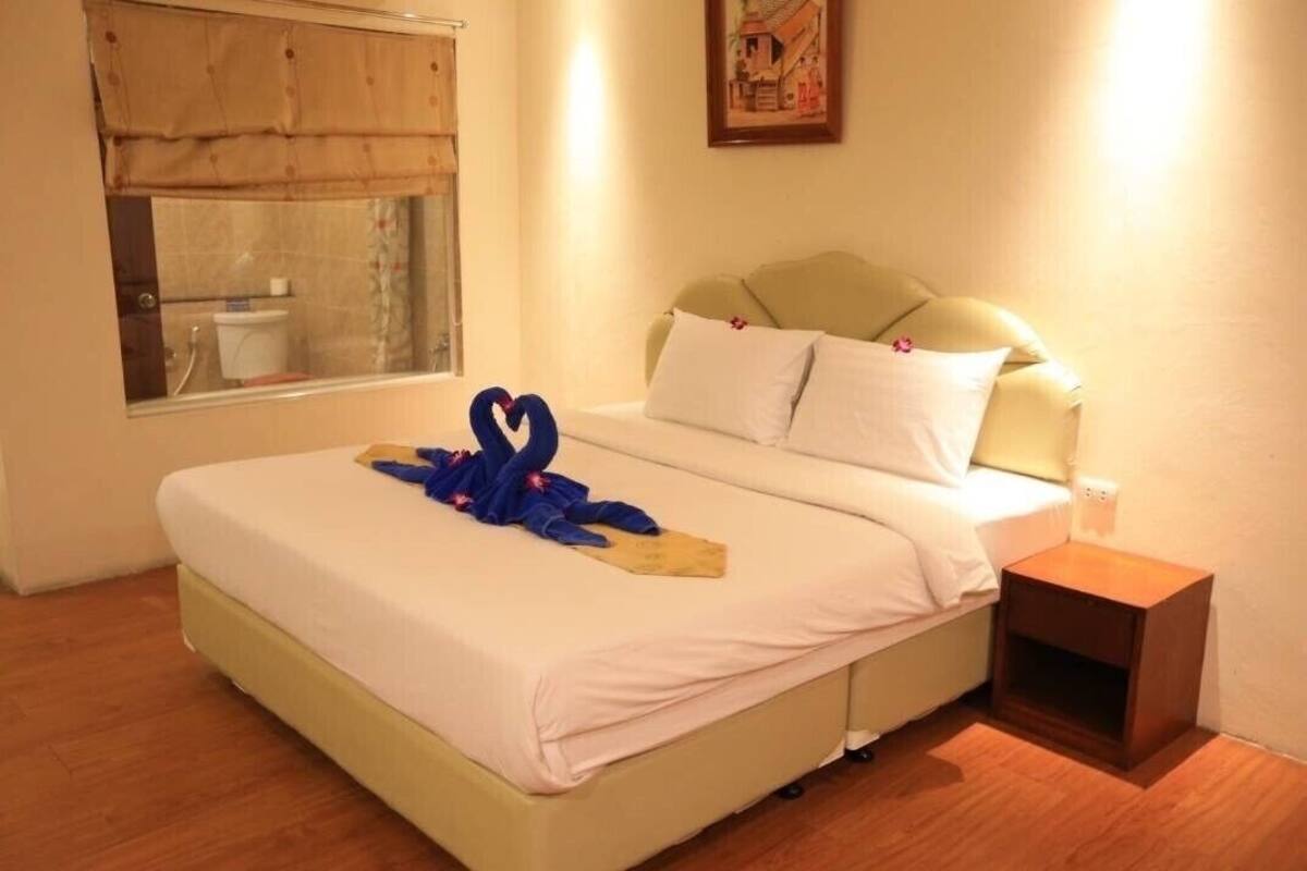 A hotel room with a bed, a bedside table, a window with a curtain, and a painting on the wall.