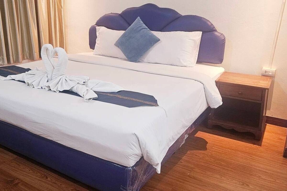 A neatly made bed with a blue headboard, a wooden nightstand, and a curtain.