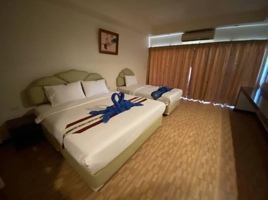 A hotel room with two beds, a wooden floor, a painting on the wall, and a window with curtains.