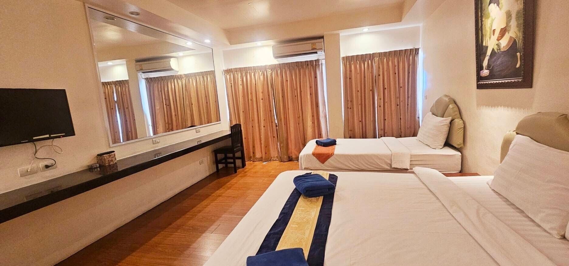 A hotel room with a bed, a desk, a chair, a television, and a large mirror.