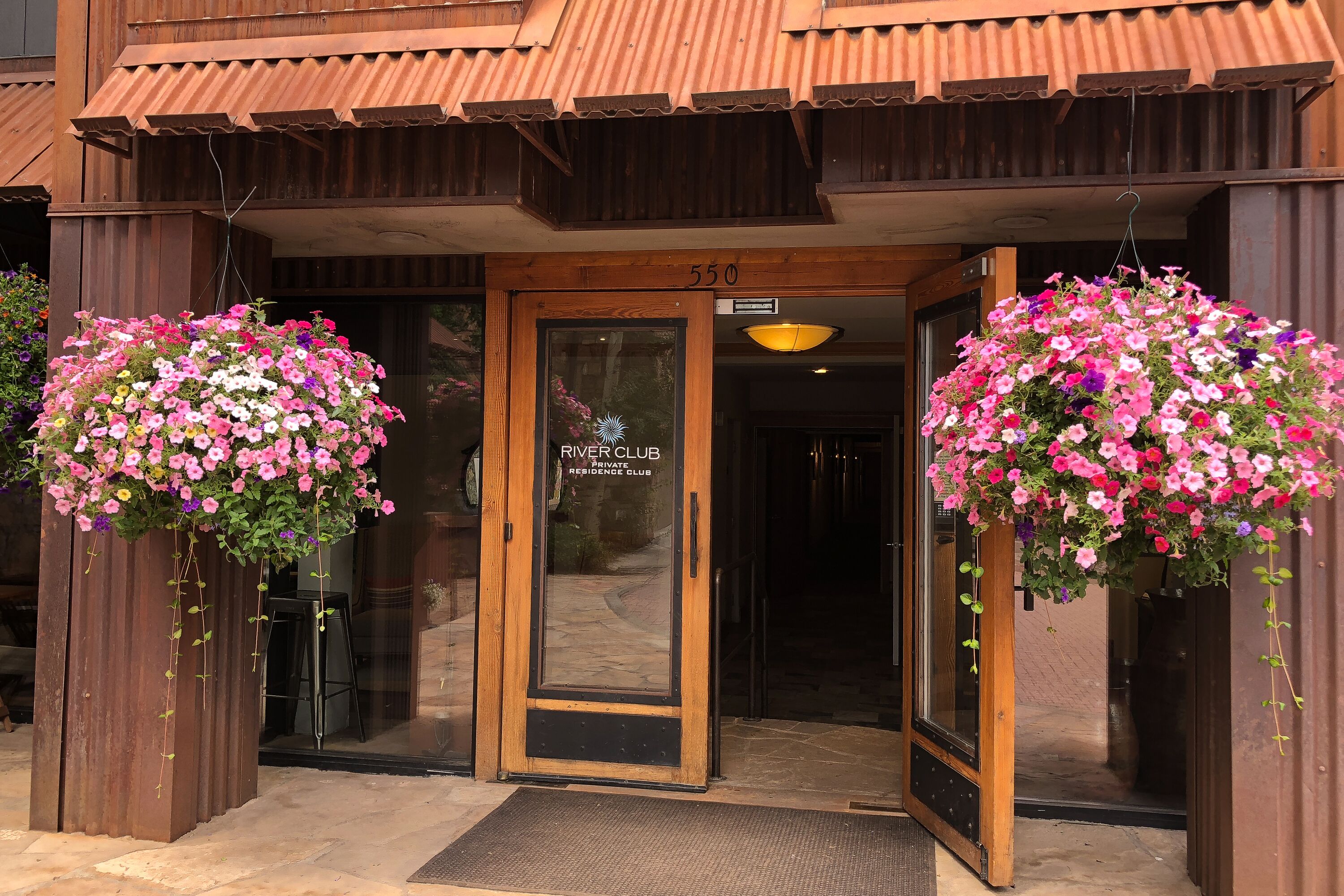 A building entrance with a wooden door, a number '550' above it, and two hanging flower baskets.