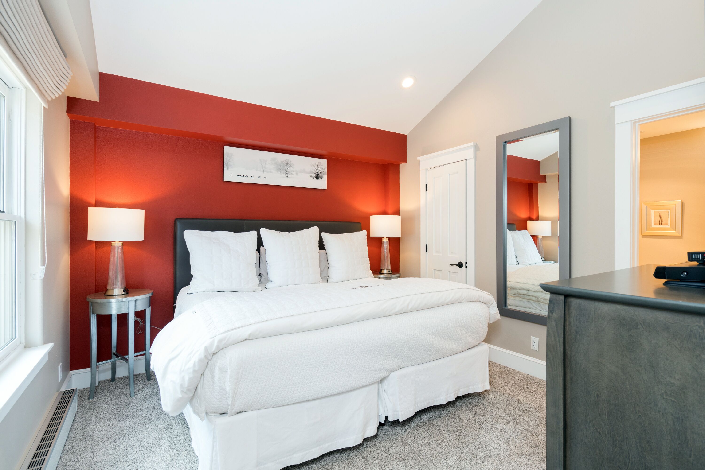Ett modernt hotellrum med en stor säng, två sänglampor, en stor spegel och ett inramat konstverk på väggen.