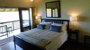 A neatly made bed with a headboard, two bedside lamps, and a large mirror on the wall. - Romantic Modern Upstairs Corner Studio with Ocean View, on the Island of Molokai (Maunaloa)