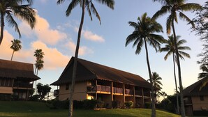 A resort with multiple-story buildings, palm trees, and a grassy lawn. - Romantic Modern Upstairs Corner Studio with Ocean View, on the Island of Molokai (Maunaloa)
