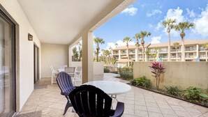 Un patio techado al aire libre con una mesa y sillas, palmeras y un edificio al fondo.
