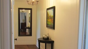 Een gang met houten vloeren, een donker houten console en decoratieve vazen, een lijstwerk schilderij en een kroonluchter.