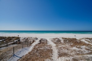 A beach with a clear sky, sandy dunes, and a wooden fence.